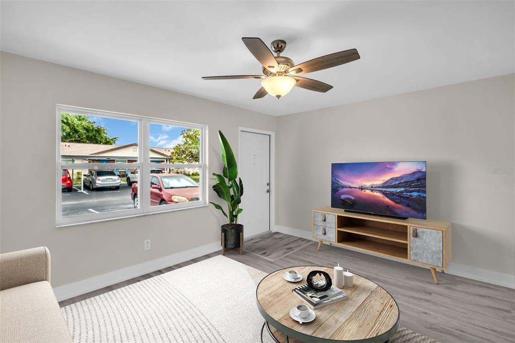 A living room features a ceiling fan, a television on a console, and a large window — 24862 US HIGHWAY 19 N UNIT 1105, CLEARWATER, FL