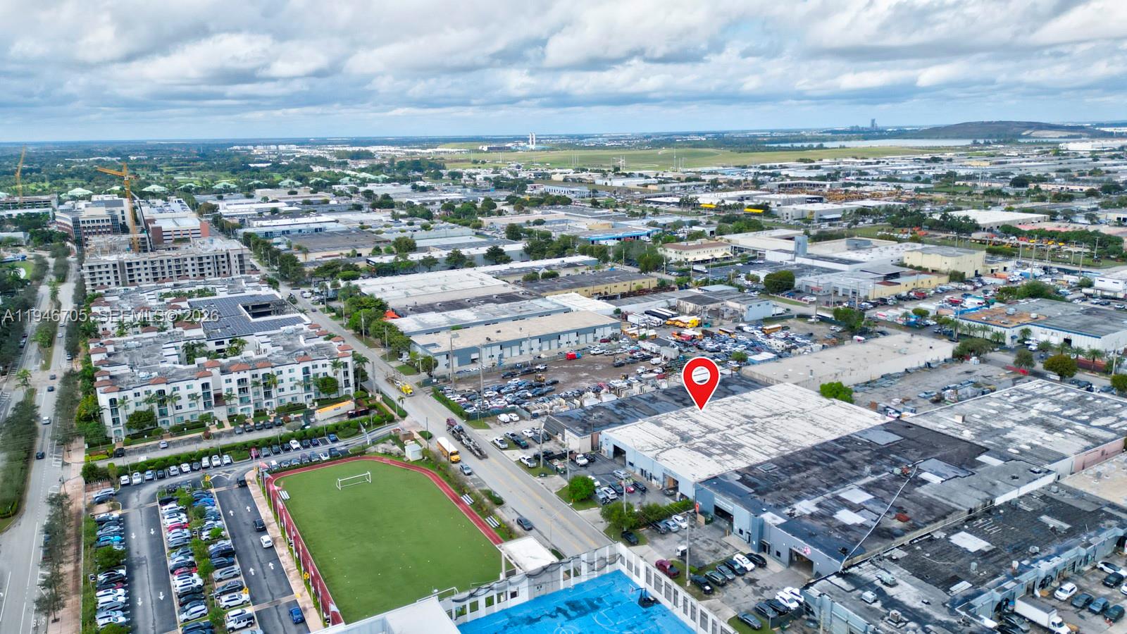 An aerial view shows a commercial warehouse building with a parking lot and soccer field — 7957 NW 54th St, Doral FL 33166, DORAL, FL