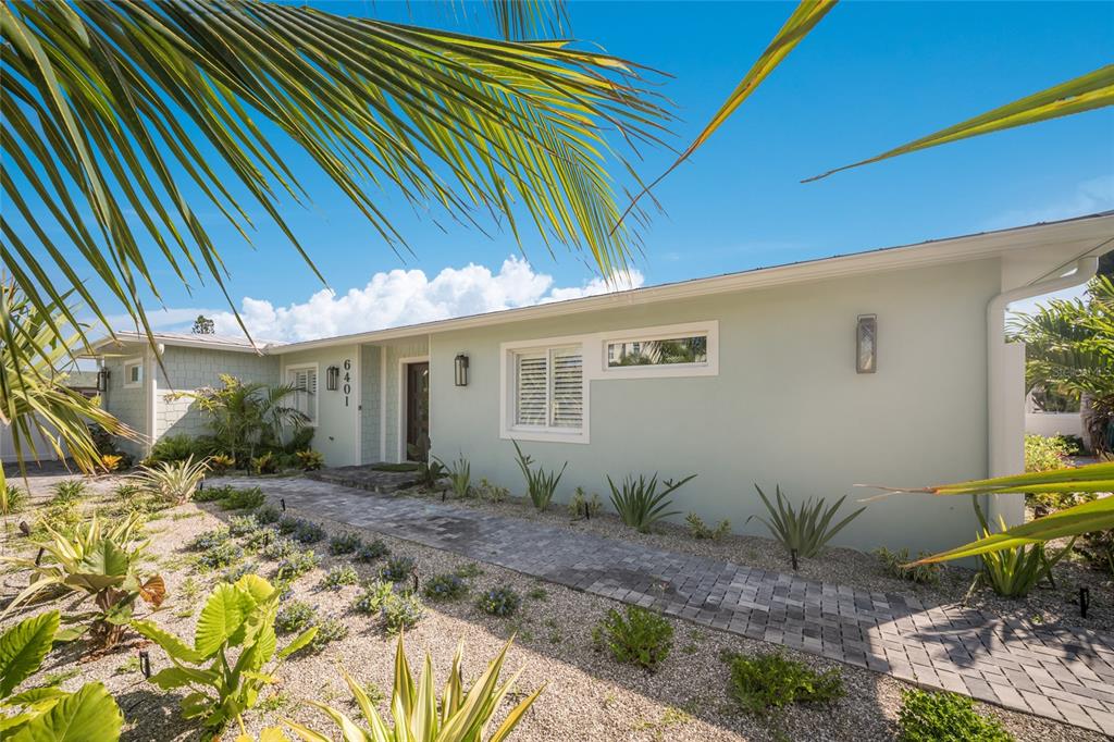 A light green single-story house features a stone walkway and tropical landscaping under a blue sky — 6401 MARINA DRIVE, HOLMES BEACH, FL