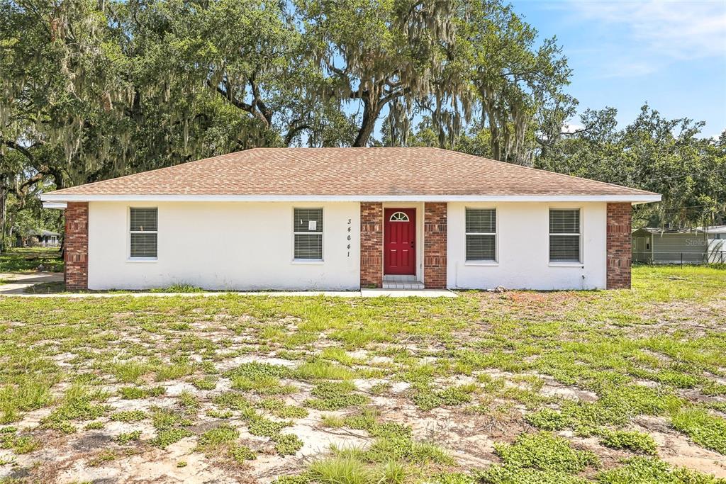 A single-story house with a red front door and brick accents sits on a grassy lot — 34641 DOGWOOD DRIVE, DADE CITY, FL