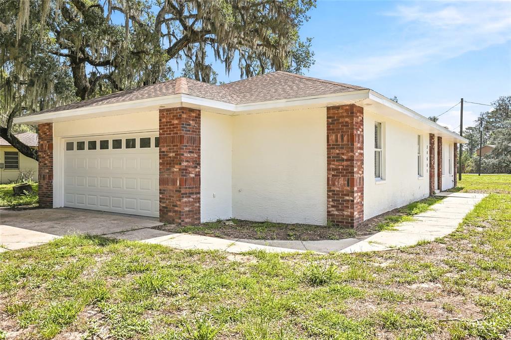 A single-story house with a white stucco exterior, brick corner accents, and a garage — 34641 DOGWOOD DRIVE, DADE CITY, FL