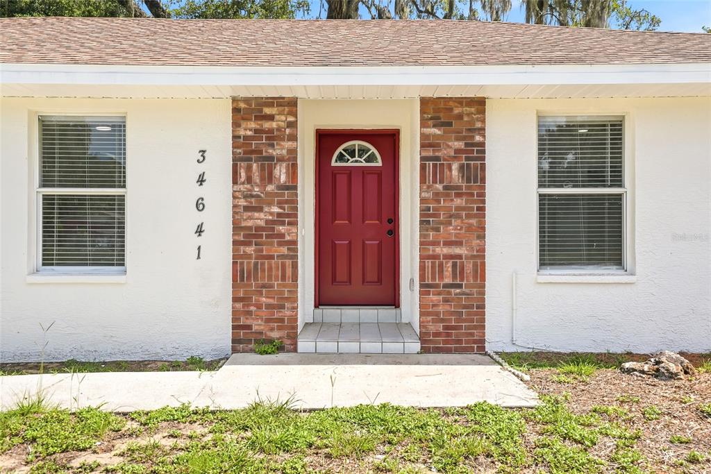 The exterior of a house features a red front door flanked by brick columns — 34641 DOGWOOD DRIVE, DADE CITY, FL