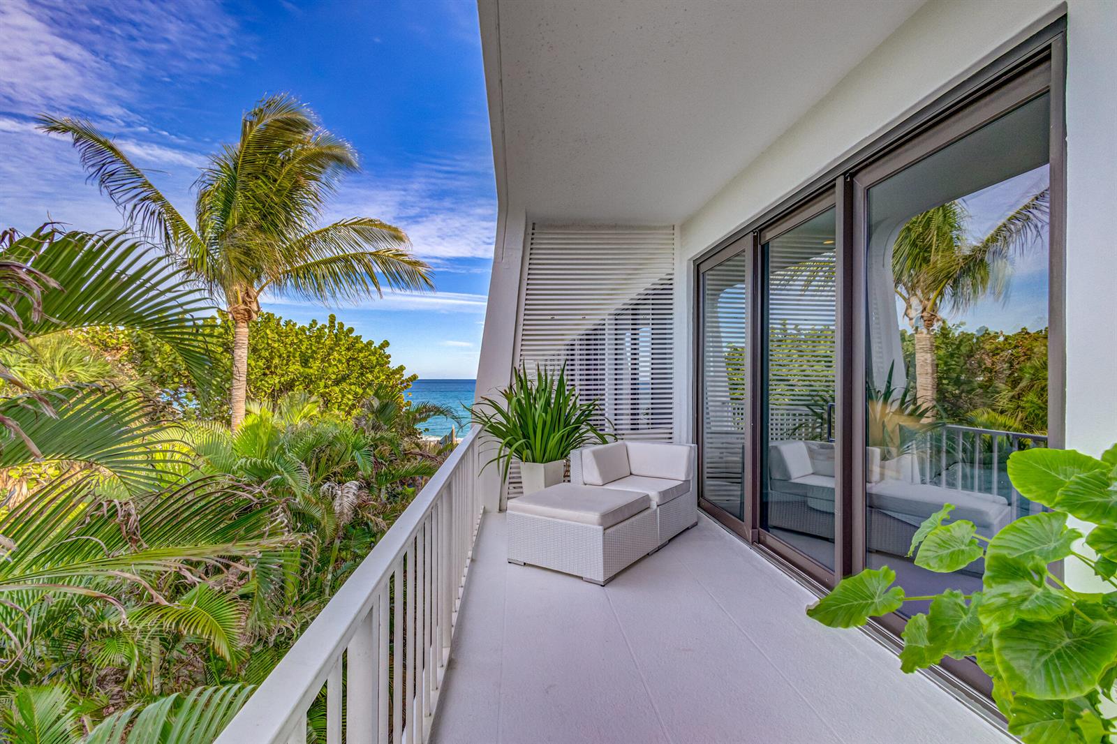 A white balcony with a lounge chair overlooks tropical foliage and the ocean — 2275 S Ocean Boulevard # 305n, Palm Beach FL 33480, PALM BEACH, FL