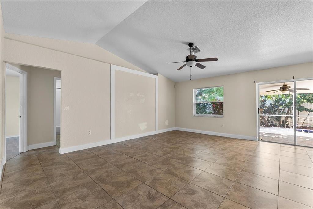 An empty living room features beige walls, tiled floors, a vaulted ceiling, and sliding doors — 307 STERLING DRIVE, WINTER HAVEN, FL