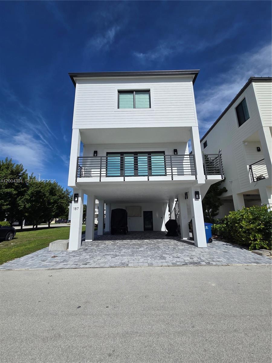 A white, elevated two-story house features a paved driveway and a balcony with railings — 94825 Overseas Hwy #187, Key Largo FL 33037, KEY LARGO, FL