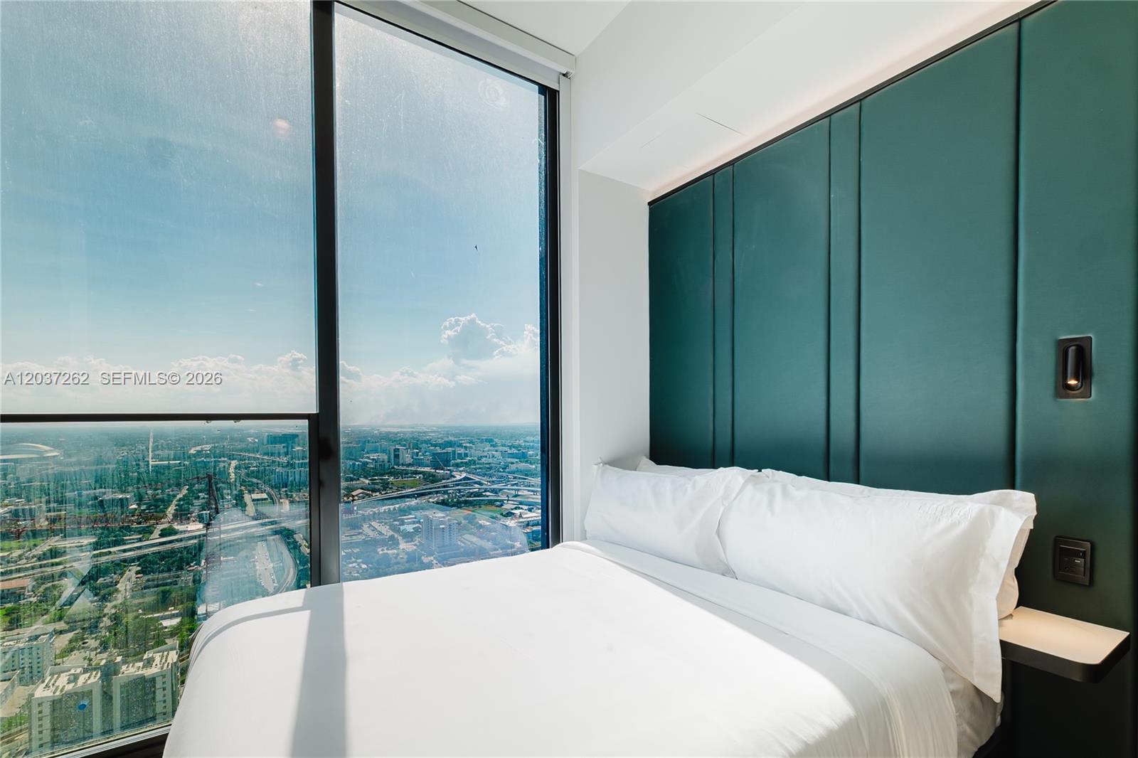 A bedroom features a bed against a dark green paneled wall with floor-to-ceiling city views — 20 NE 11th st # 4807B, Miami FL 33132, MIAMI, FL
