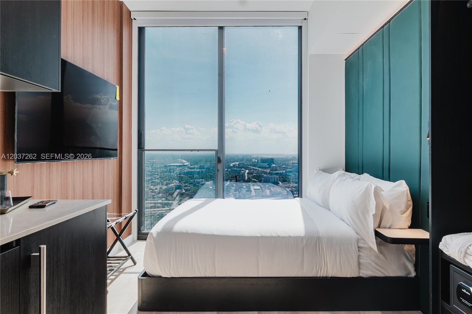 A modern bedroom features a bed against a teal headboard and floor-to-ceiling city views — 20 NE 11th st # 4807B, Miami FL 33132, MIAMI, FL