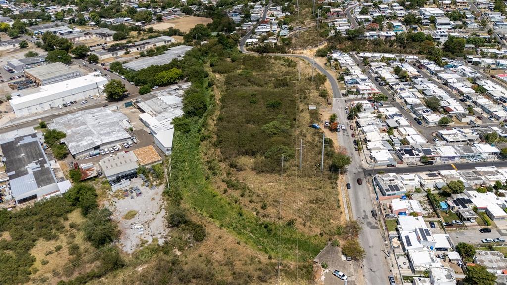 An aerial view shows a vacant, overgrown lot situated between a residential neighborhood and industrial buildings — 1 REPARTO INDUSTRIAL, PONCE, PR