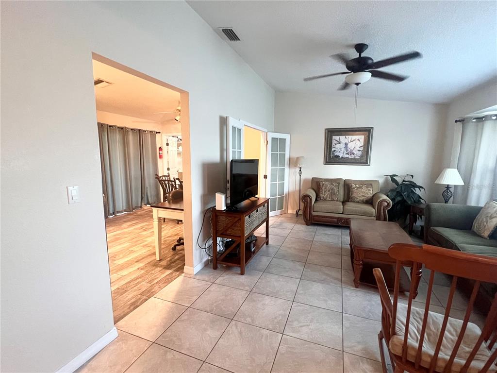 A living room with tile floors, a ceiling fan, and a view into an adjacent room — 20362 EMERALD AVENUE, PORT CHARLOTTE, FL