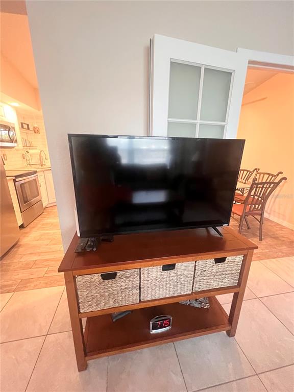 A television sits on a wooden console table with woven baskets in a tiled room — 20362 EMERALD AVENUE, PORT CHARLOTTE, FL