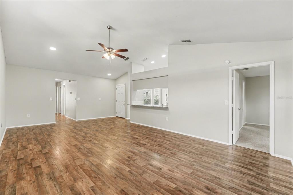 A spacious living room with wood-look flooring, a ceiling fan, and a kitchen pass-through window — 638 LAKE DEXTER CIRCLE, WINTER HAVEN, FL