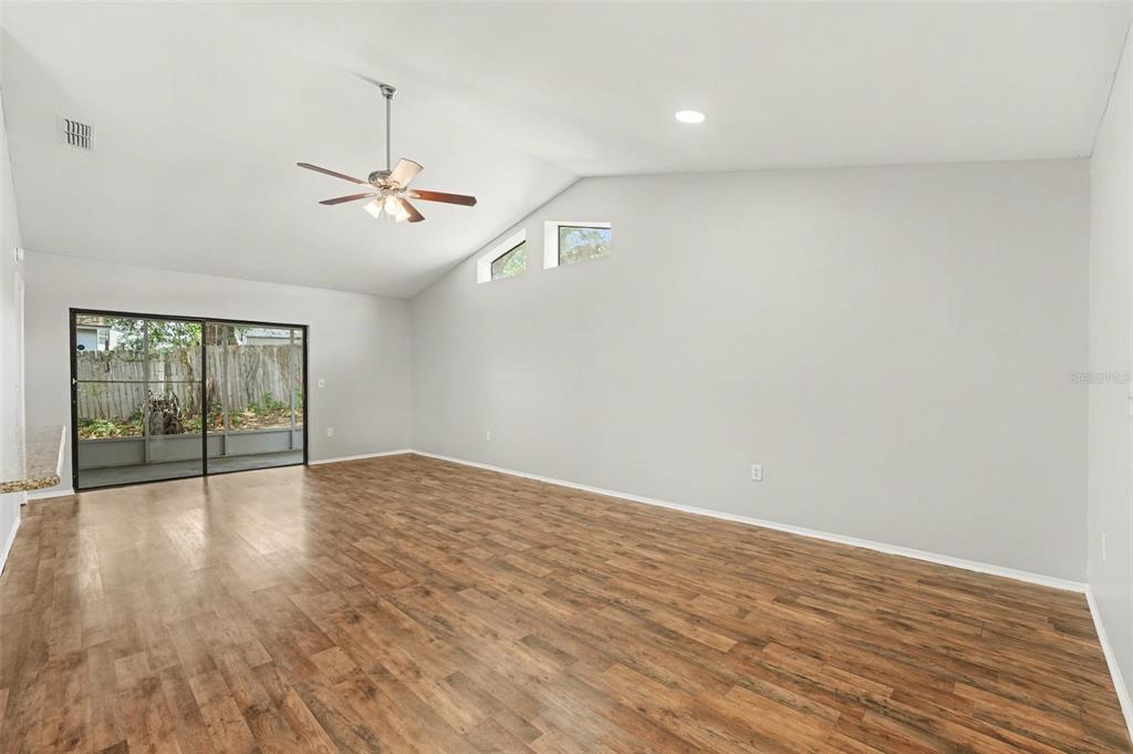 An empty living room features vaulted ceilings, wood-look flooring, a ceiling fan, and sliding glass doors — 638 LAKE DEXTER CIRCLE, WINTER HAVEN, FL