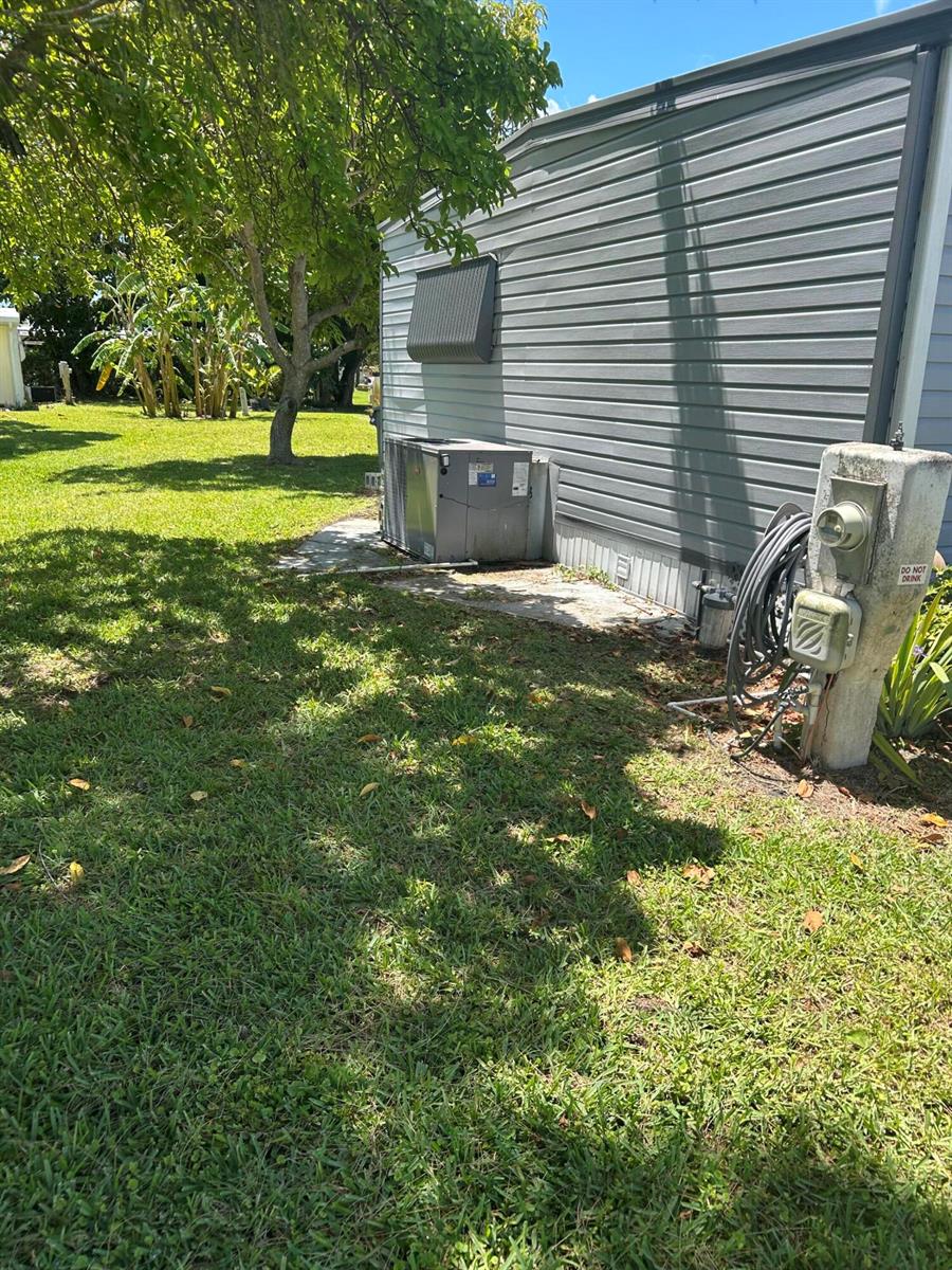 The exterior of a mobile home features gray siding, an AC unit, and a utility post — 8628 Duke Court E, Boynton Beach FL 33436, BOYNTON BEACH, FL