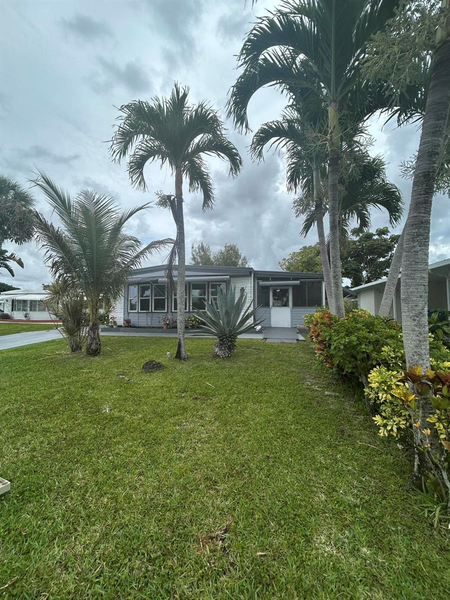 A single-story mobile home with a gray exterior sits behind a lawn and palm trees — 8628 Duke Court E, Boynton Beach FL 33436, BOYNTON BEACH, FL