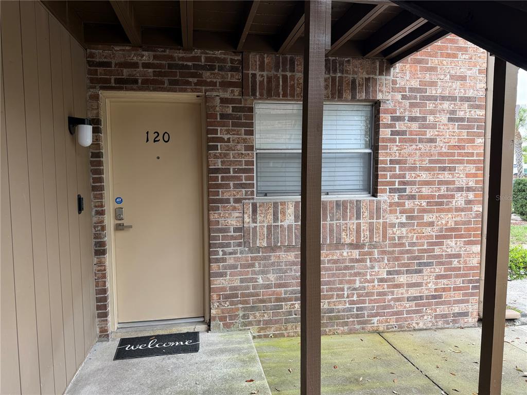 A tan front door marked 120 sits beside a brick wall and a window — 10485 CARROLLBROOK CIRCLE UNIT 120, TAMPA, FL