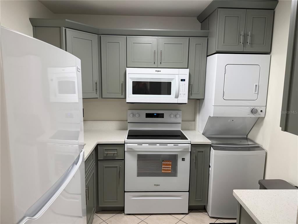 A kitchen features gray cabinets, white appliances, a stacked washer-dryer unit, and light countertops — 10485 CARROLLBROOK CIRCLE UNIT 120, TAMPA, FL