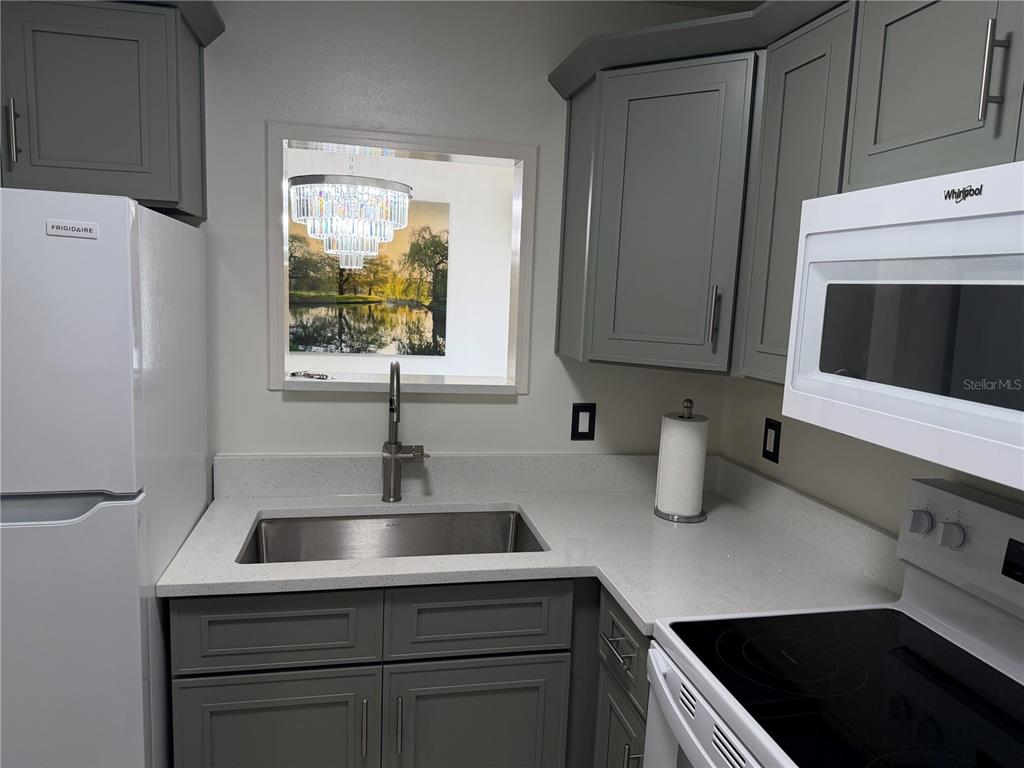 A kitchen features gray cabinets, white countertops, a stainless steel sink, and a pass-through window — 10485 CARROLLBROOK CIRCLE UNIT 120, TAMPA, FL