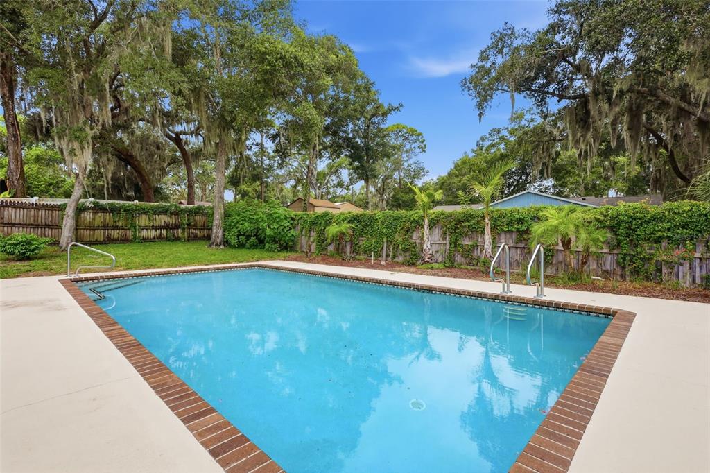 A rectangular swimming pool with a brick border sits in a grassy backyard with trees — 226 COUNCIL BLUFFS DRIVE, DELTONA, FL