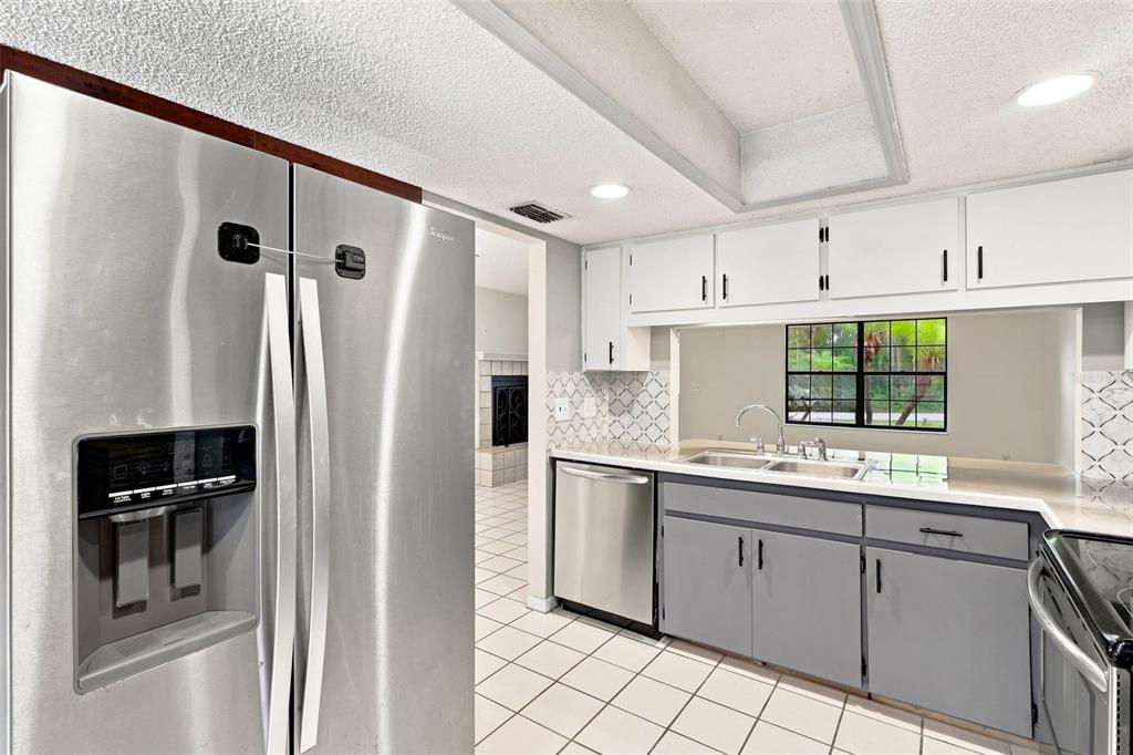 A kitchen features stainless steel appliances, gray lower cabinets, white upper cabinets, and tiled flooring — 226 COUNCIL BLUFFS DRIVE, DELTONA, FL