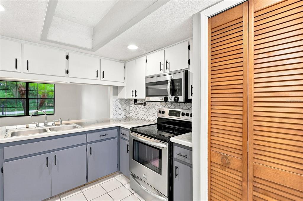 A kitchen features blue lower cabinets, white upper cabinets, stainless steel appliances, and tile flooring — 226 COUNCIL BLUFFS DRIVE, DELTONA, FL