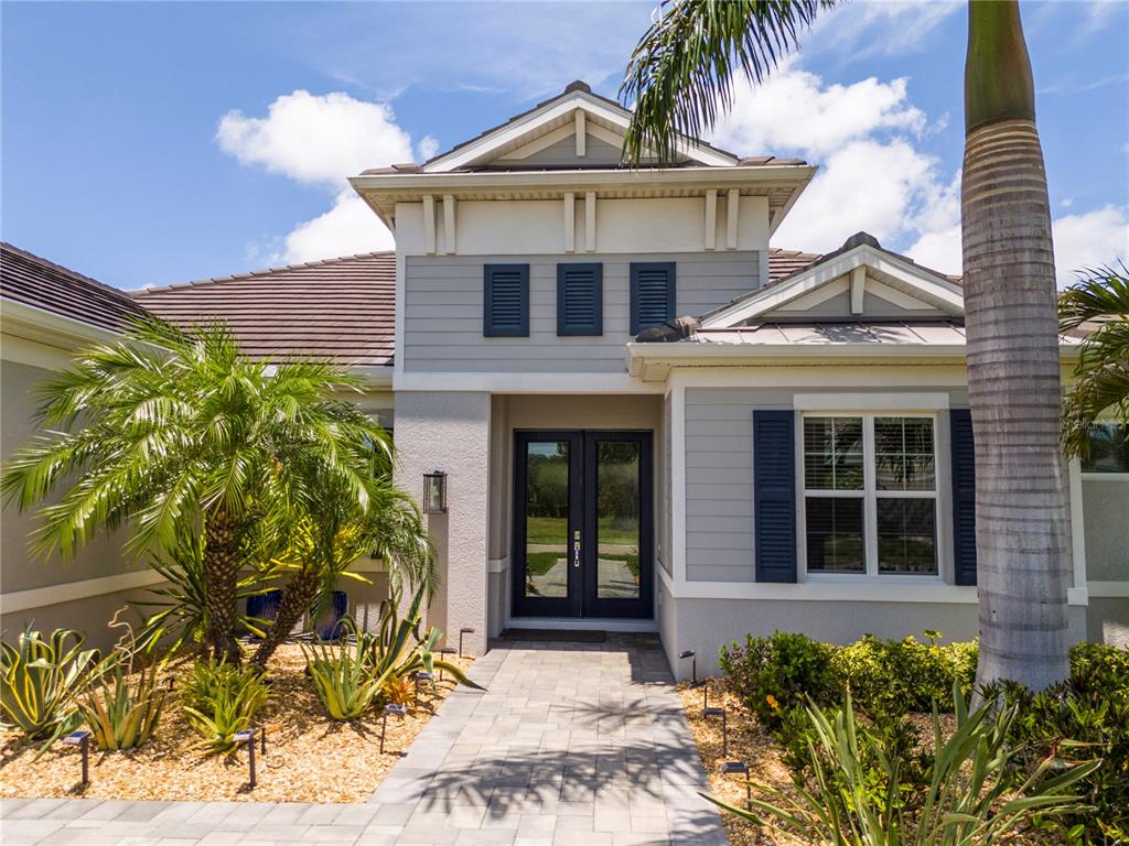 A gray house exterior features a double-door entrance, a stone walkway, and tropical landscaping — 7181 RYEDALE COURT, SARASOTA, FL