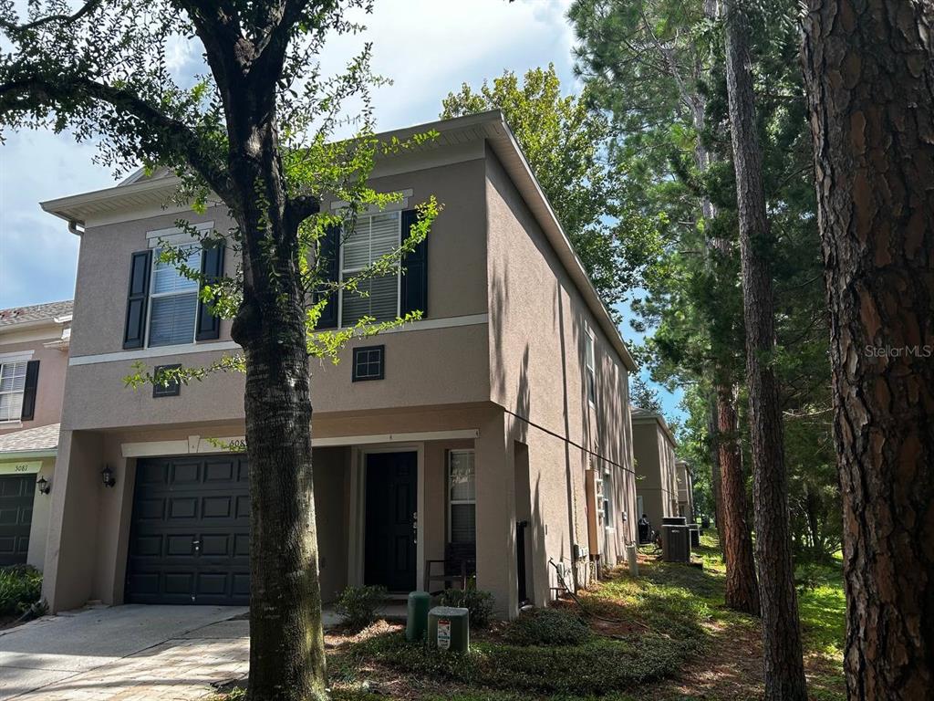 A two-story tan stucco townhouse with a dark garage door and black window shutters — 5085 KINGSCREST LANE, OVIEDO, FL