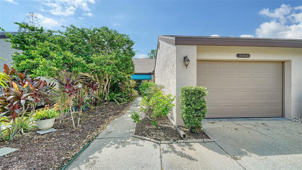 A concrete entryway features a teal awning, a screen door, and surrounding tropical landscaping — 5956 CLUBSIDE DRIVE UNIT 7651, SARASOTA, FL