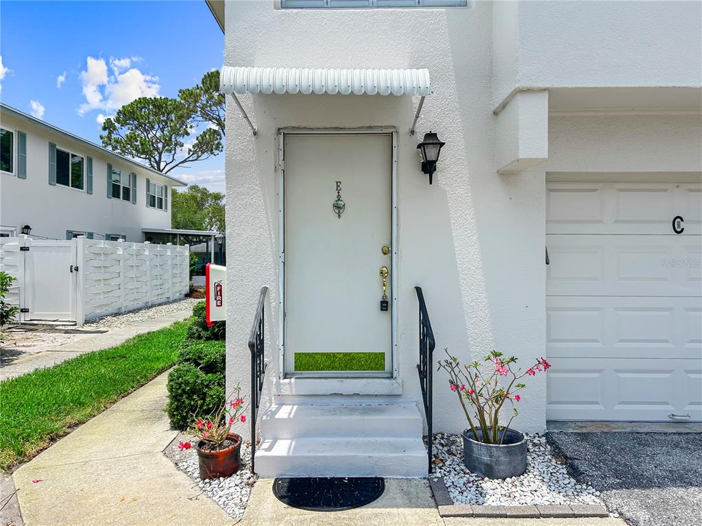 A white front door with a metal awning and a small adjacent garage door — 3265 40TH WAY S UNIT E, ST PETERSBURG, FL