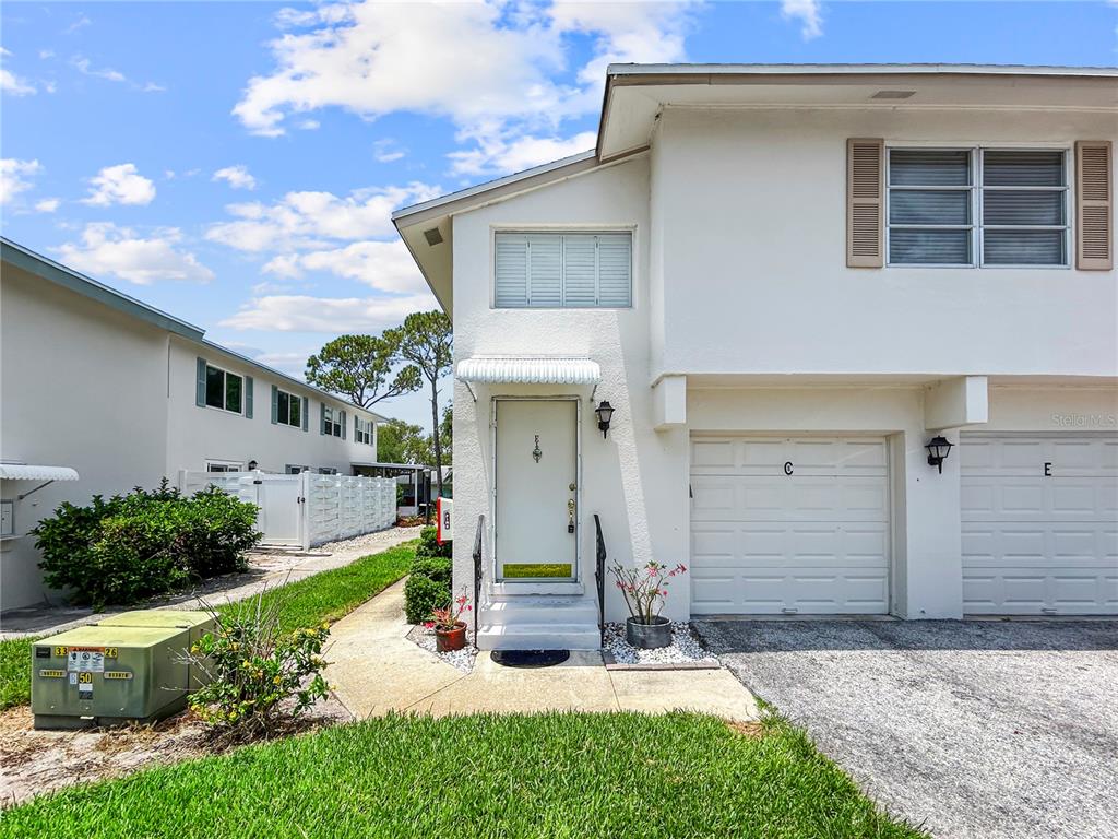 A two-story white townhouse exterior features a front door, a garage, and a small lawn — 3265 40TH WAY S UNIT E, ST PETERSBURG, FL