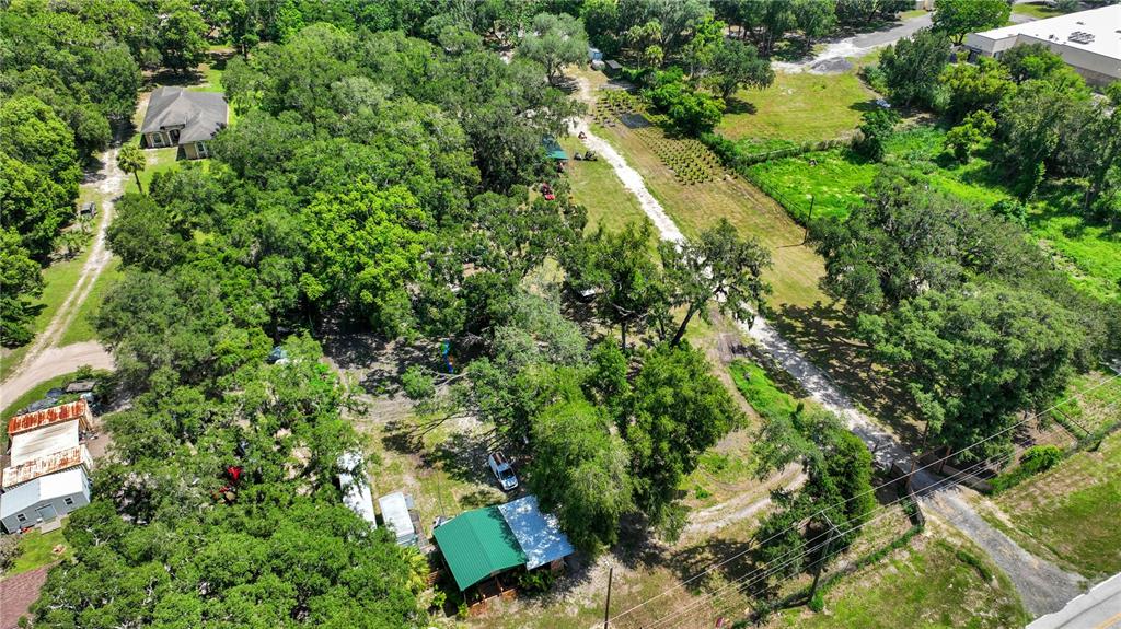 An aerial view shows a wooded property with several small buildings, outbuildings, and dirt paths — 9922 ROCKHILL ROAD, THONOTOSASSA, FL