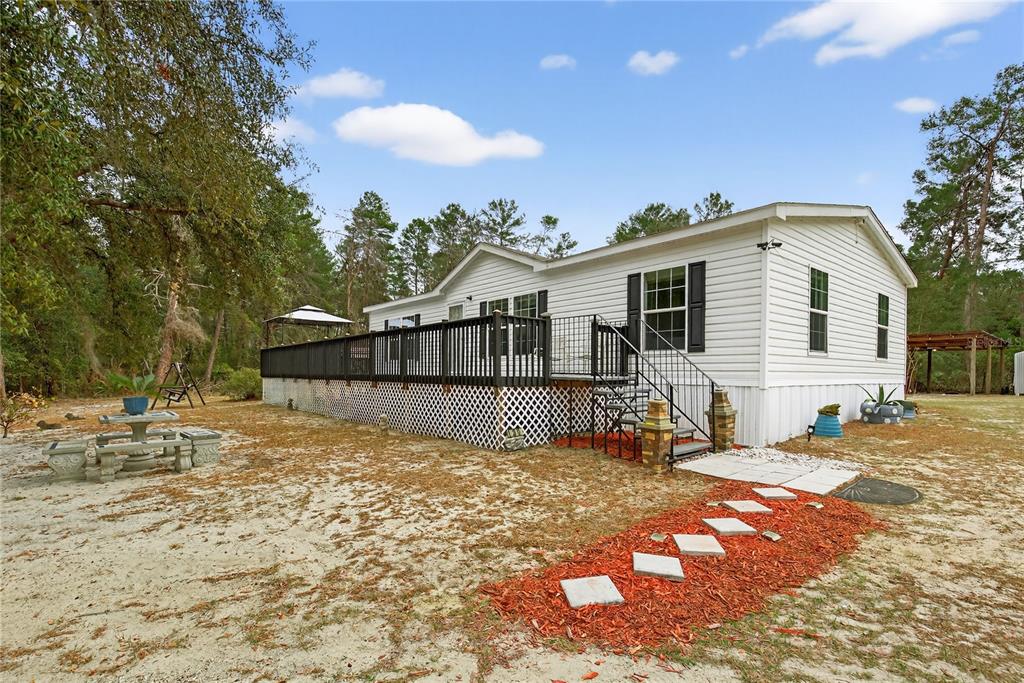 A white manufactured home features a large black deck and a stone walkway — 117 STODDARD ROAD, CRESCENT CITY, FL