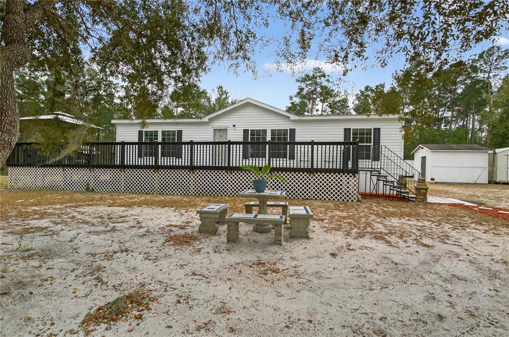 A white manufactured home features a large black deck with lattice skirting and a patio set — 117 STODDARD ROAD, CRESCENT CITY, FL