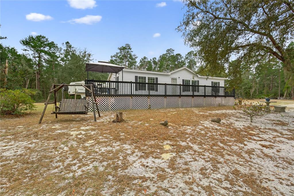 A white manufactured home features a large wooden deck with a gazebo and swing set — 117 STODDARD ROAD, CRESCENT CITY, FL