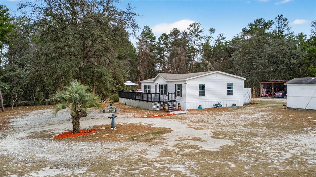 A white manufactured home with a large wooden deck sits on a sandy, wooded lot — 117 STODDARD ROAD, CRESCENT CITY, FL