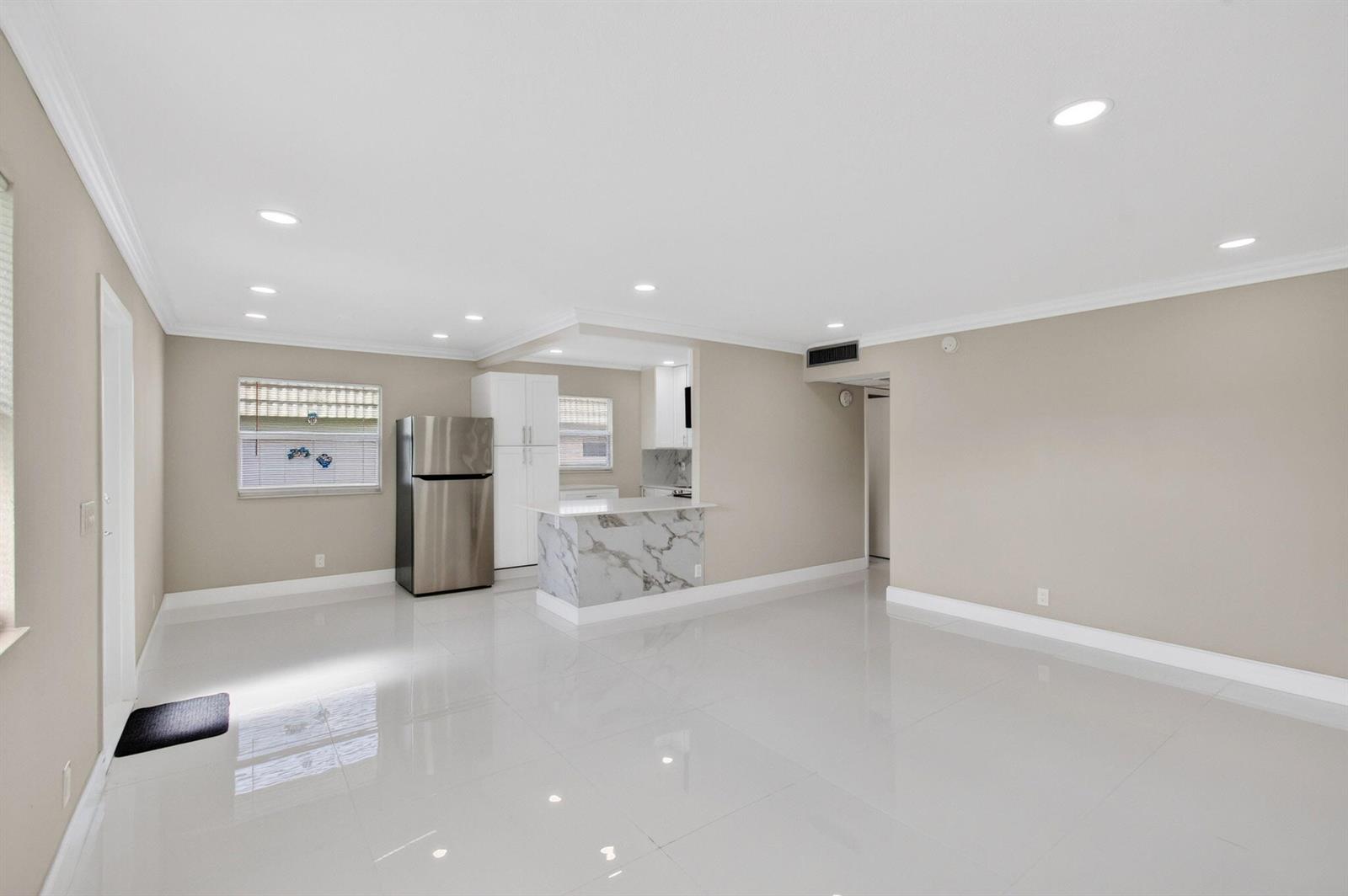A bright, open-concept living area features white tile floors, beige walls, and a marble-topped kitchen — 429 Flanders I, Delray Beach FL 33484, DELRAY BEACH, FL