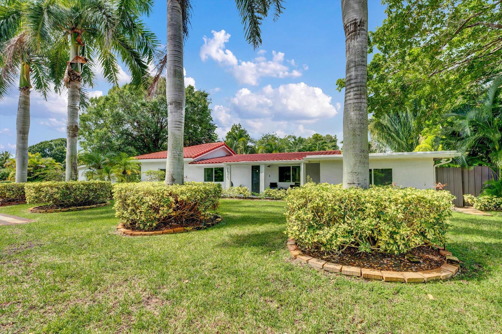 A white single-story house with a red tile roof sits behind palm trees and shrubs — 2633 NE 3rd Avenue, Wilton Manors FL 33334, WILTON MANORS, FL
