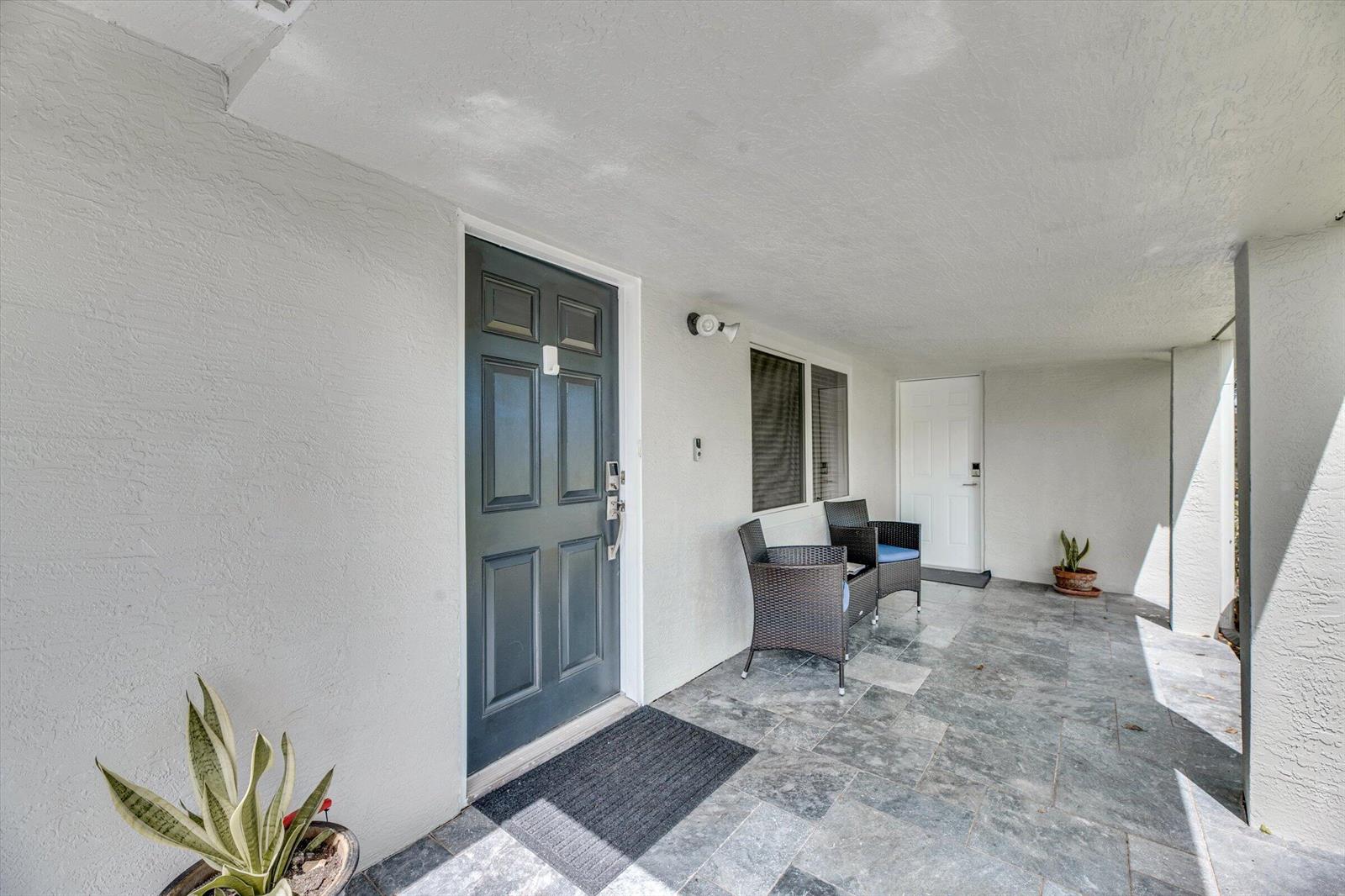 A covered patio features gray stone flooring, two wicker chairs, and two exterior doors — 2633 NE 3rd Avenue, Wilton Manors FL 33334, WILTON MANORS, FL