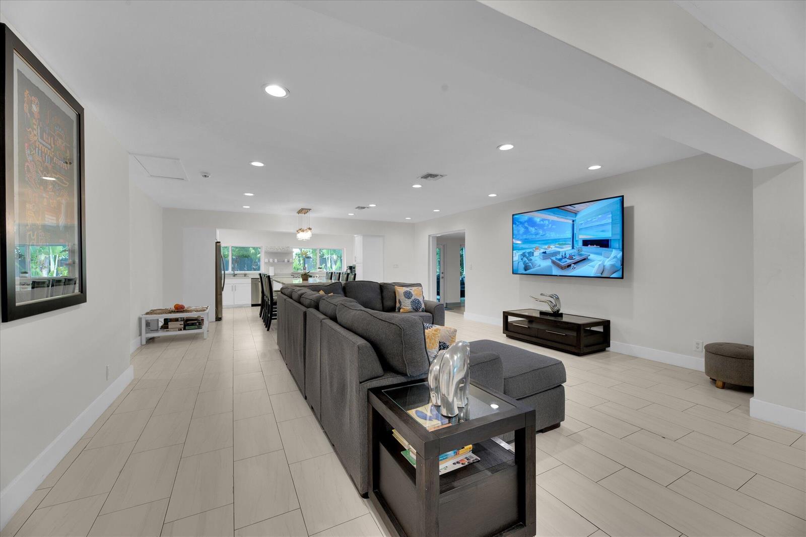 A spacious living room with light tile floors, a large gray sectional, and wall-mounted television — 2633 NE 3rd Avenue, Wilton Manors FL 33334, WILTON MANORS, FL