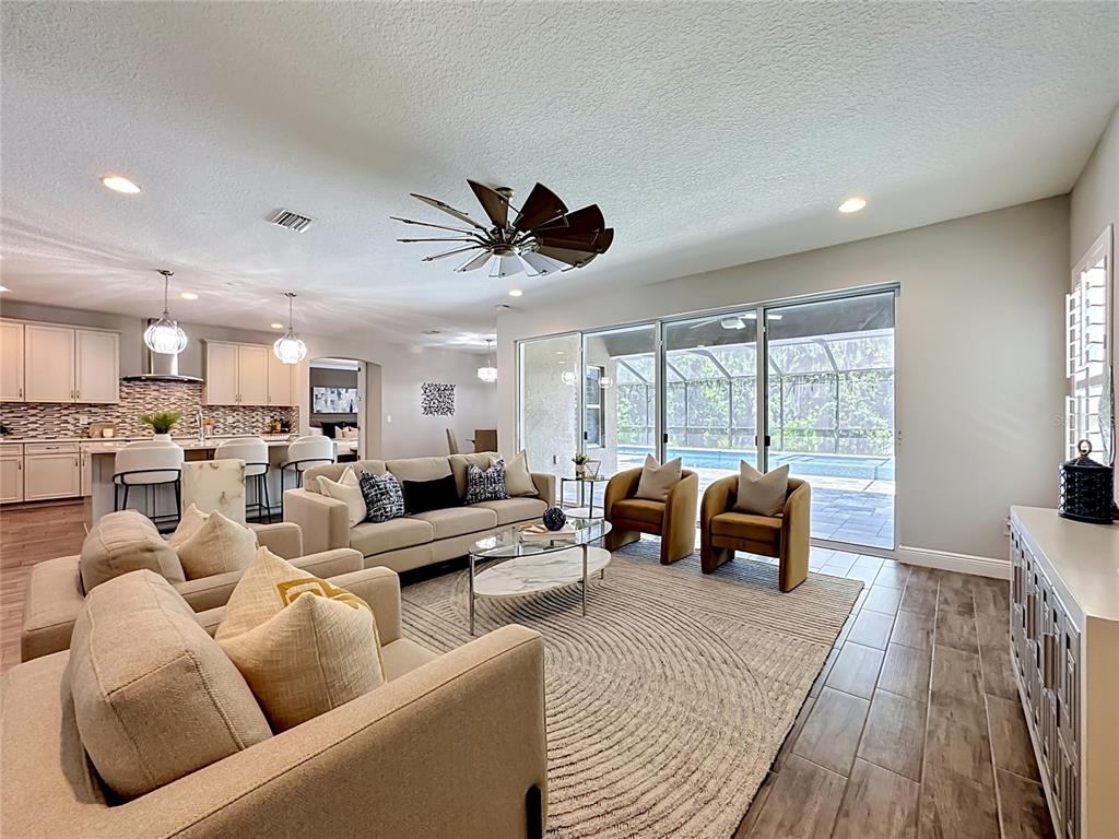 An open-concept living room features a kitchen, dining area, and sliding doors to a pool — 13231 WILDFLOWER MEADOW DRIVE, RIVERVIEW, FL