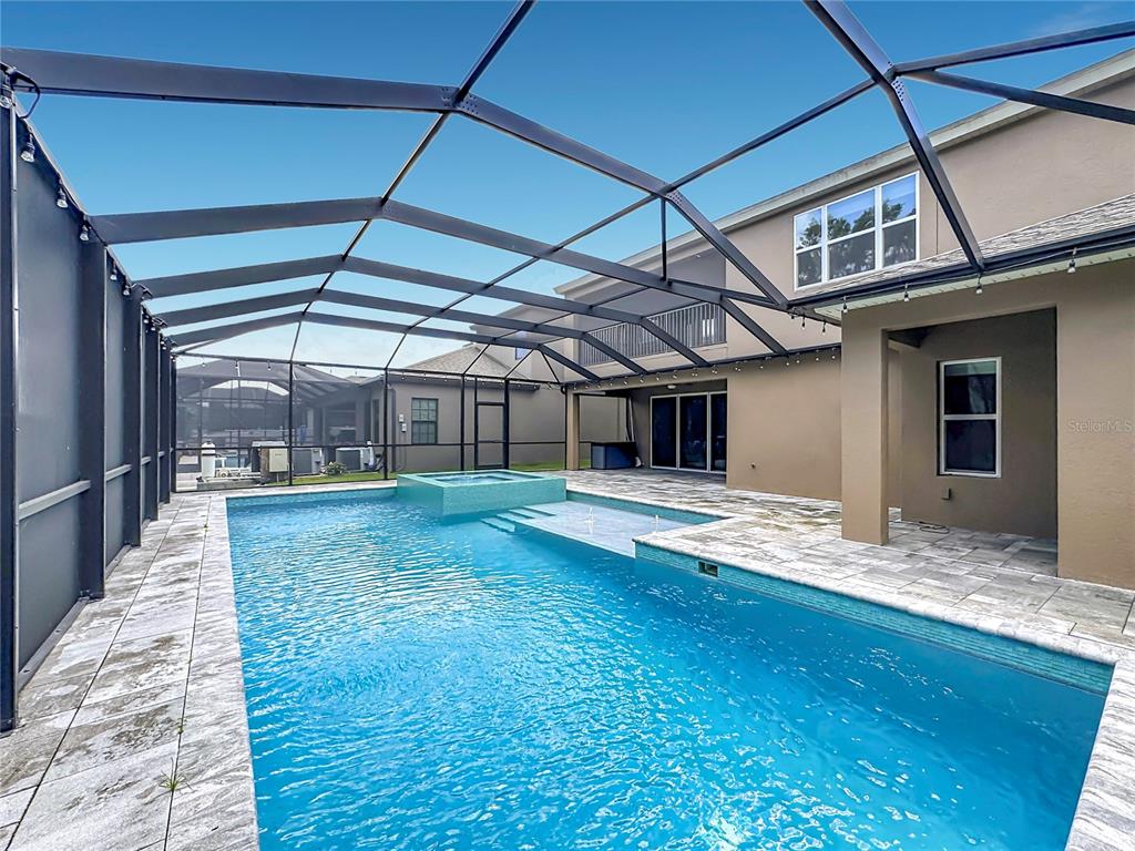 A swimming pool with a spa and tanning ledge sits inside a screened-in patio area — 13231 WILDFLOWER MEADOW DRIVE, RIVERVIEW, FL