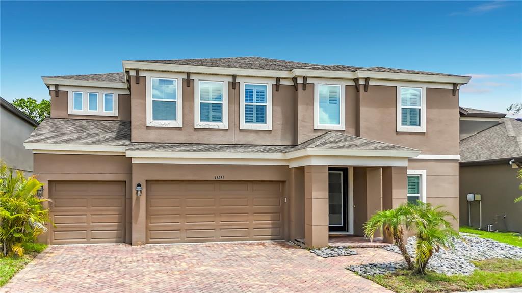 A two-story house with a brown stucco exterior, a three-car garage, and a paved driveway — 13231 WILDFLOWER MEADOW DRIVE, RIVERVIEW, FL