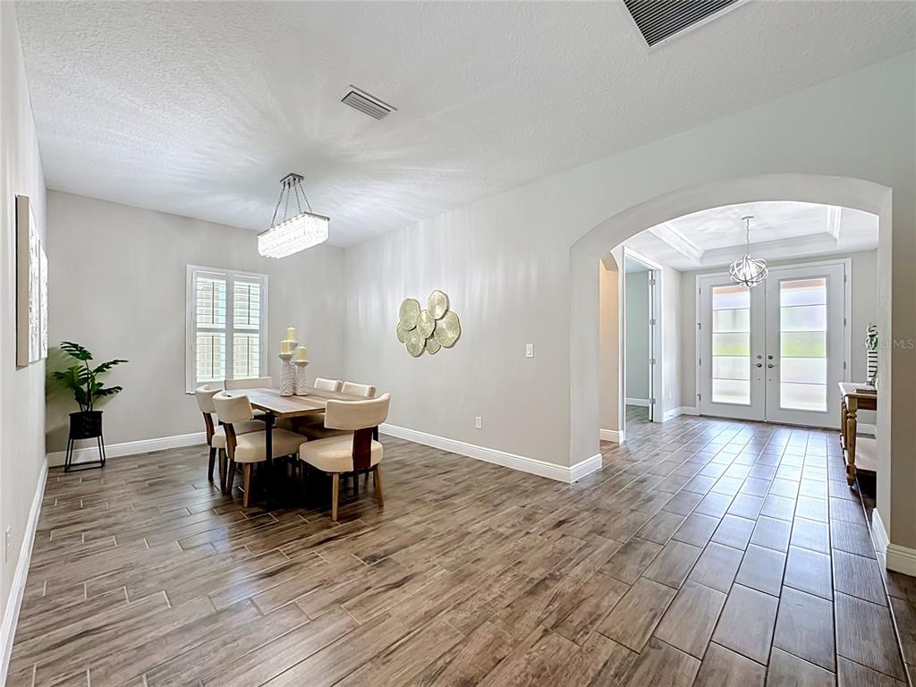 A dining room with wood-look tile floors, a crystal chandelier, and an arched entryway — 13231 WILDFLOWER MEADOW DRIVE, RIVERVIEW, FL