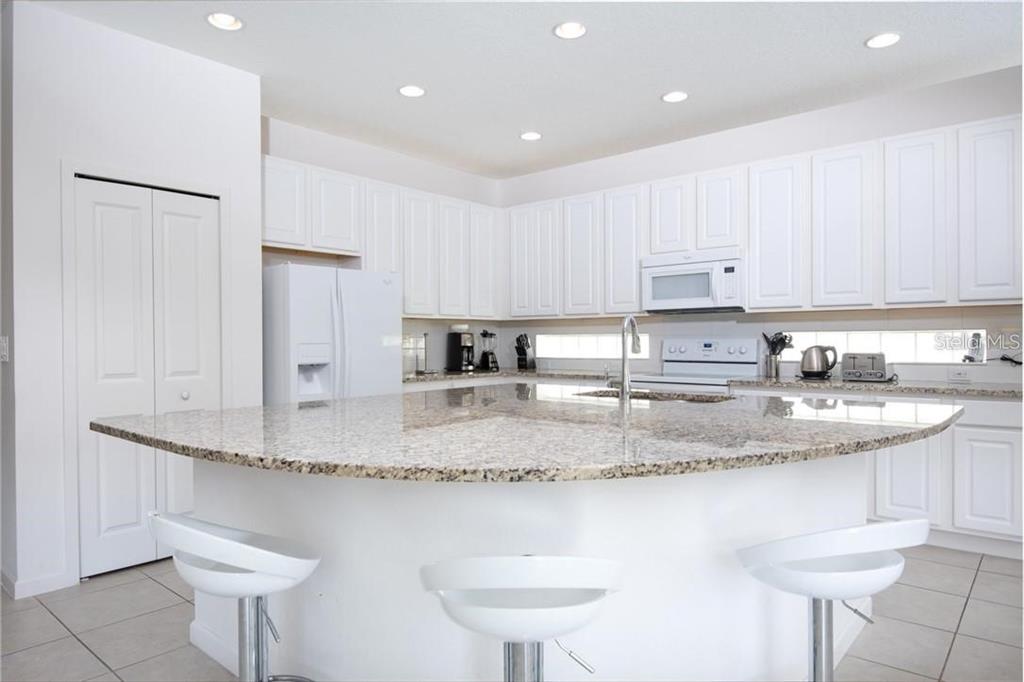 A kitchen with white cabinets, a curved granite island, and three white bar stools — 3850 OAKVILLE AVENUE, KISSIMMEE, FL