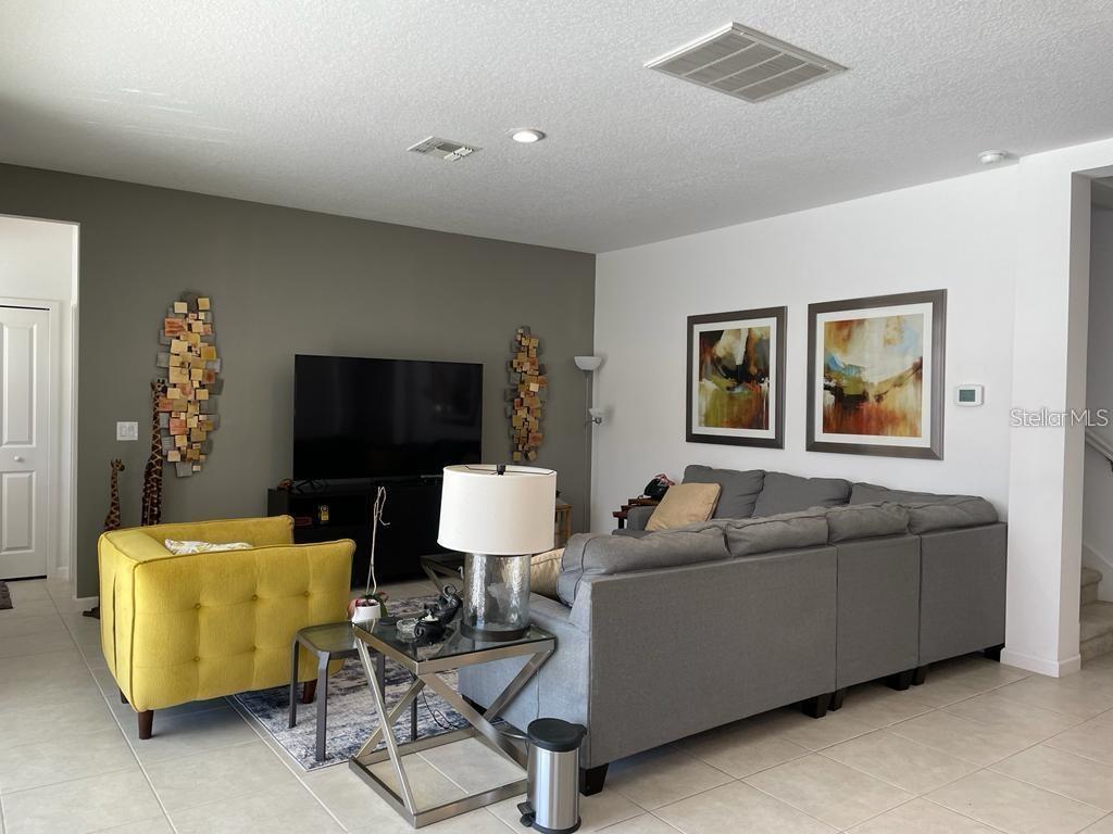 A living room features a gray sectional sofa, a yellow armchair, and a television — 3850 OAKVILLE AVENUE, KISSIMMEE, FL
