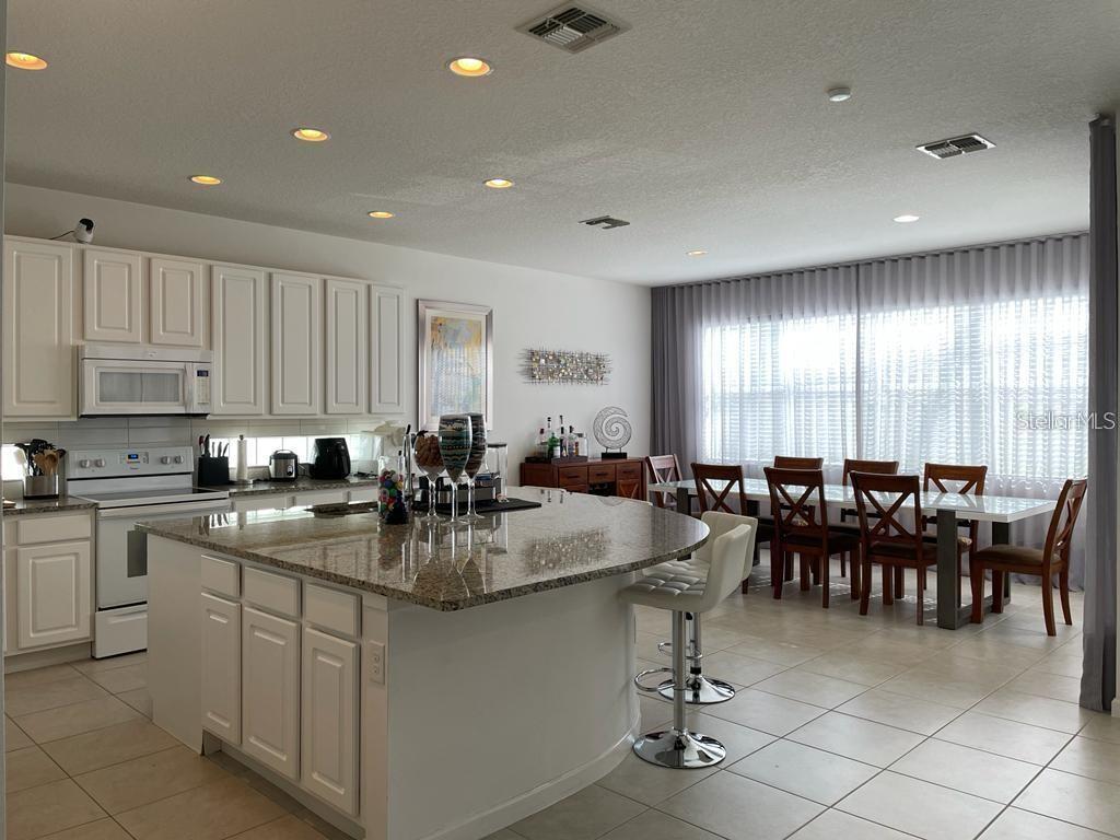 A kitchen with white cabinets, a granite island, and an adjacent dining area — 3850 OAKVILLE AVENUE, KISSIMMEE, FL