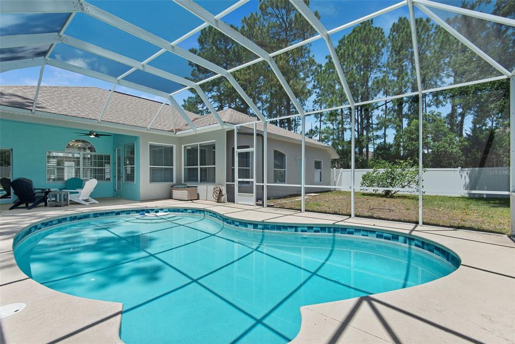 A swimming pool with a screen enclosure sits in the backyard of a residential home — 6 BURRELL PLACE, PALM COAST, FL