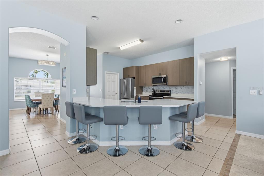 A kitchen features a curved breakfast bar with five gray stools and light-colored cabinetry — 6 BURRELL PLACE, PALM COAST, FL