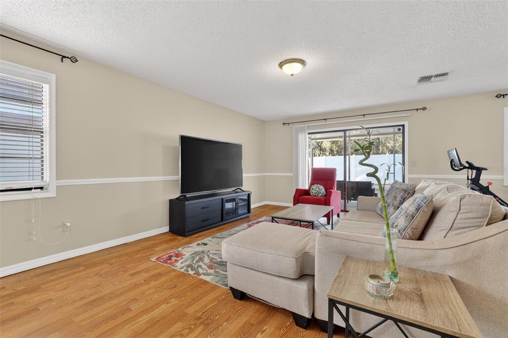 A living room features hardwood floors, a beige sectional sofa, a television, and sliding doors — 5215 CORVETTE DRIVE, TAMPA, FL
