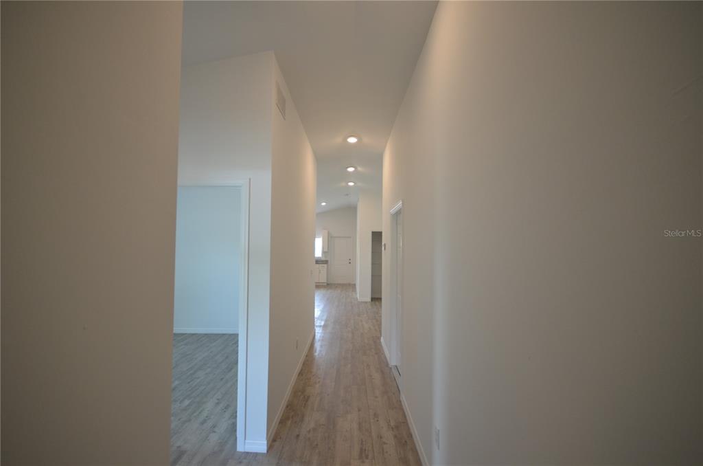 A hallway with light wood-look flooring leads toward a kitchen area with white cabinets — 2225 CARVER AVENUE, FORT MYERS, FL