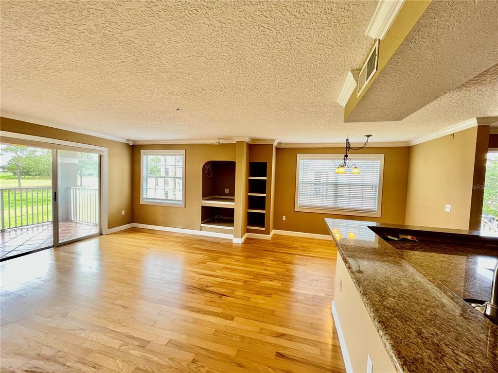 An open-concept living area features hardwood floors, a built-in shelving unit, and a granite-topped breakfast bar — 13827 FAIRWAY ISLAND DRIVE UNIT 1228, ORLANDO, FL